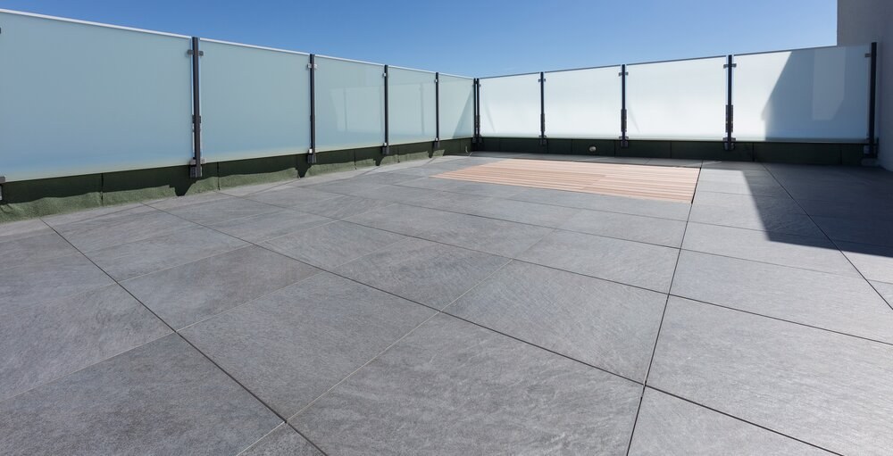 Balkon mit großformatigen grauen Fliesen und Glasbrüstung